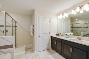 A modern bathroom with a glass shower enclosure, a large vanity with dual sinks, and a mirror with integrated lighting. - 6 Bedroom 6 Bathroom Villa (Davenport)