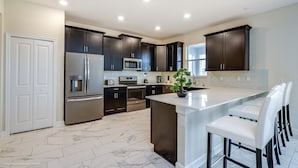 A modern kitchen with dark cabinetry, stainless steel appliances, and a central island with bar stools. - 6 Bedroom 6 Bathroom Villa (Davenport)