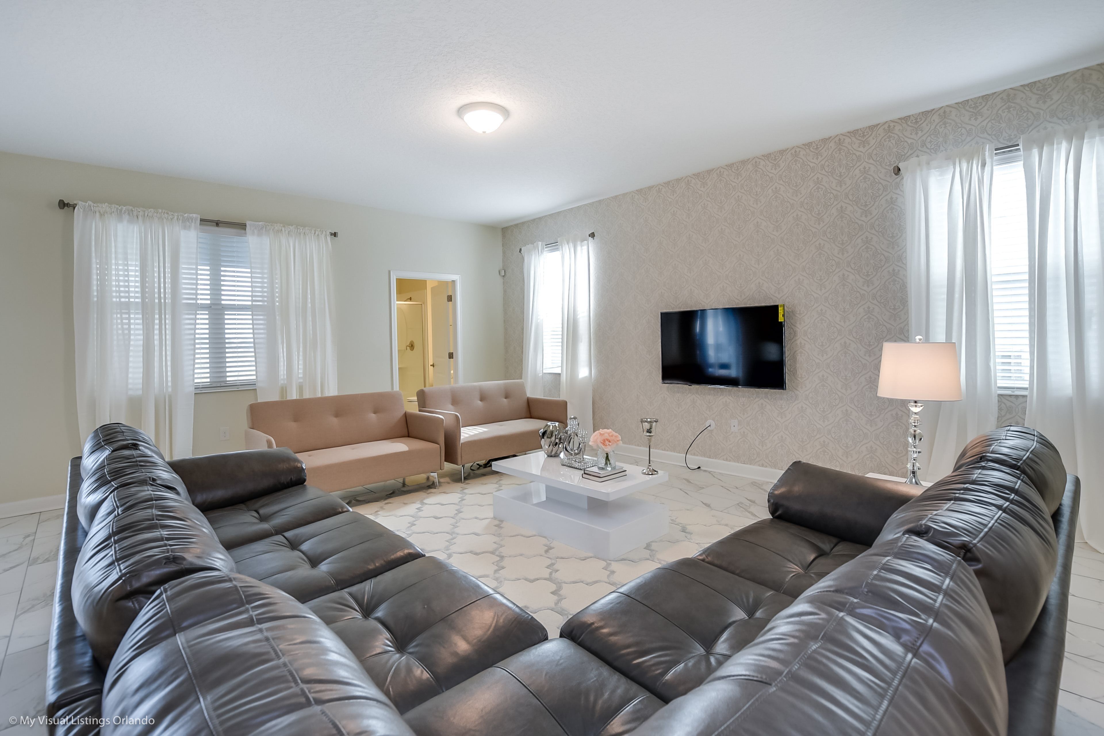 A modern living room with a large sectional sofa, a coffee table, and a flat-screen TV on the wall.