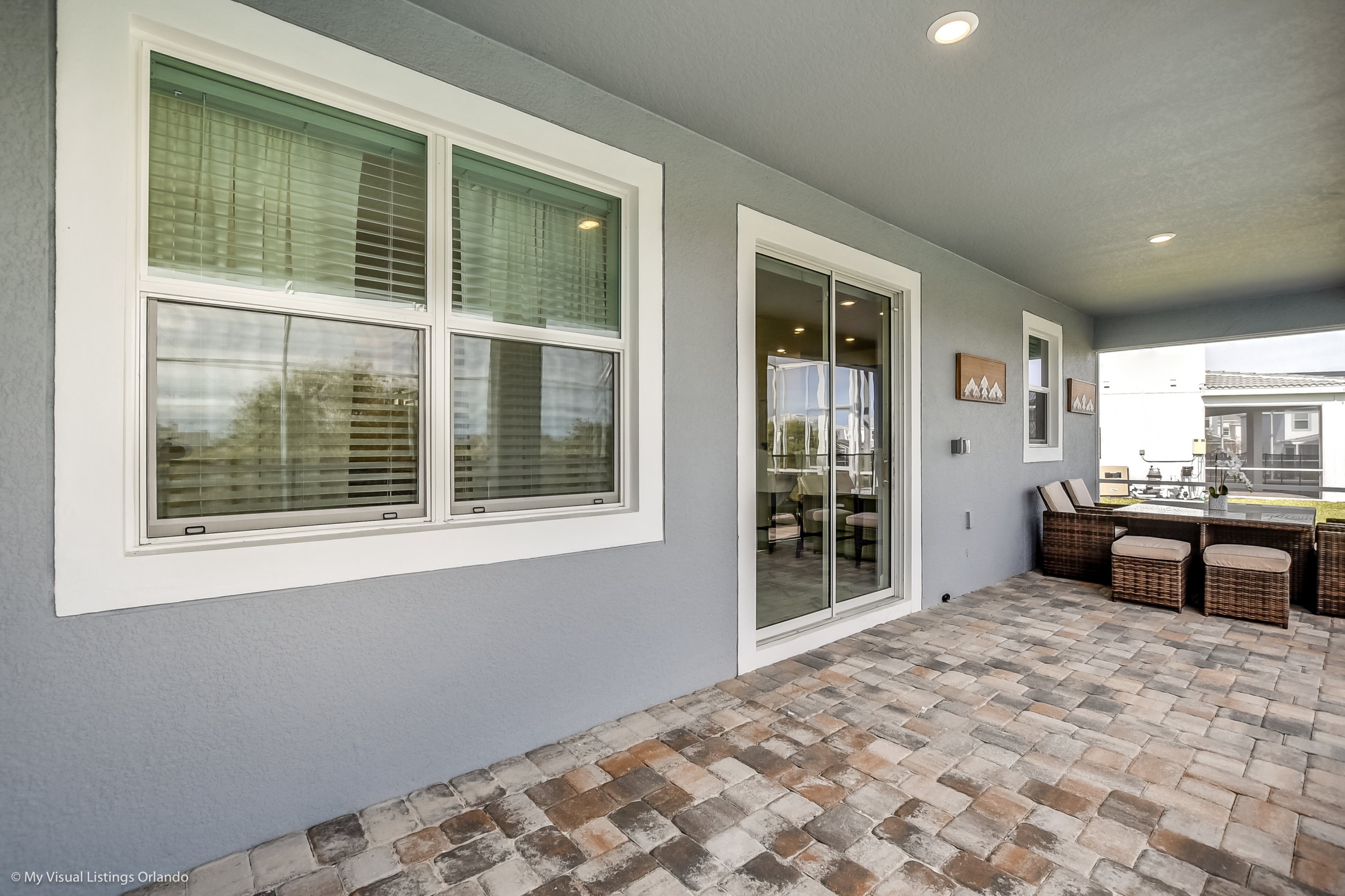 A covered patio with a brick floor and a dining area with wicker furniture.