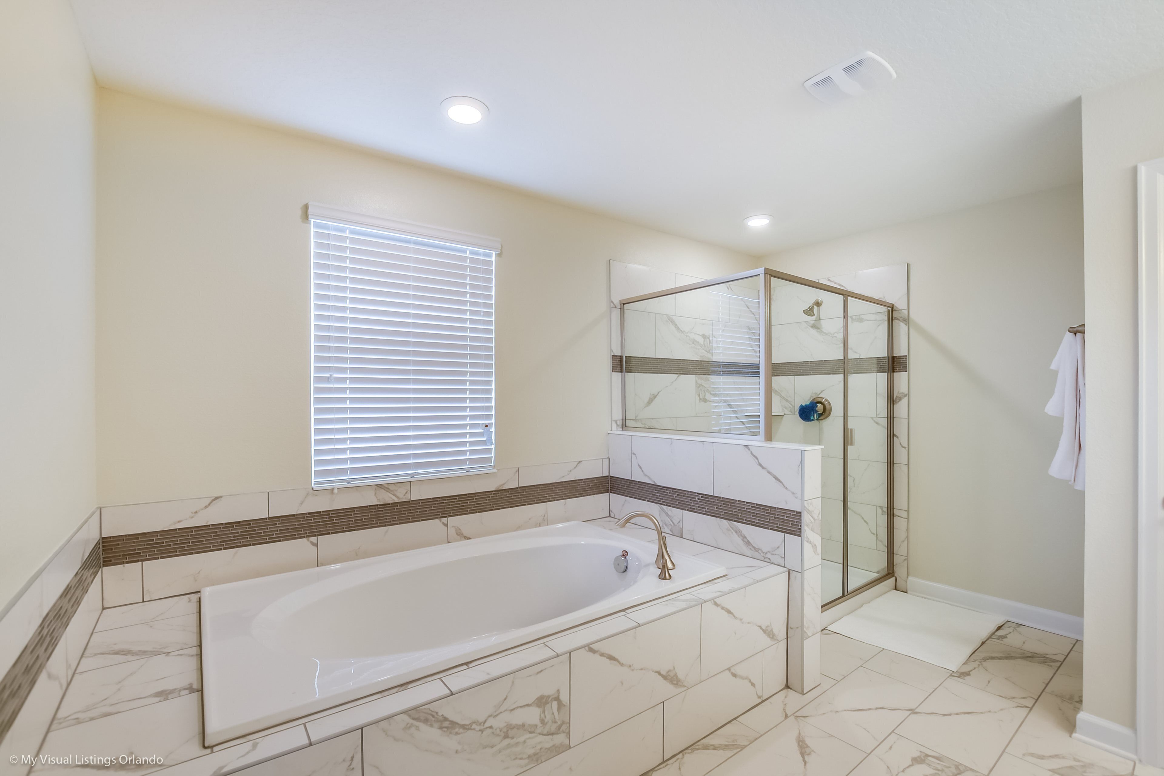 Ein modernes Badezimmer mit einer großen Badewanne, einer Duschkabine aus Glas und einem Fenster mit Jalousien.