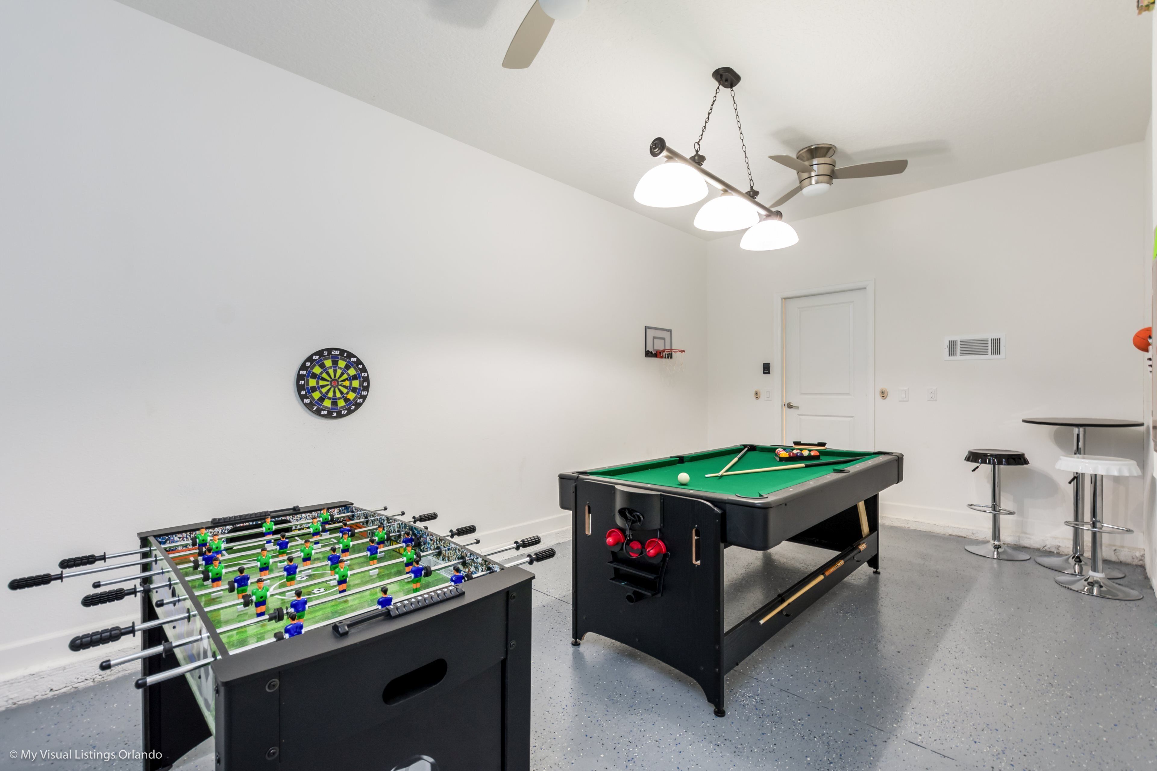 A room with a foosball table, a pool table, and a dartboard.