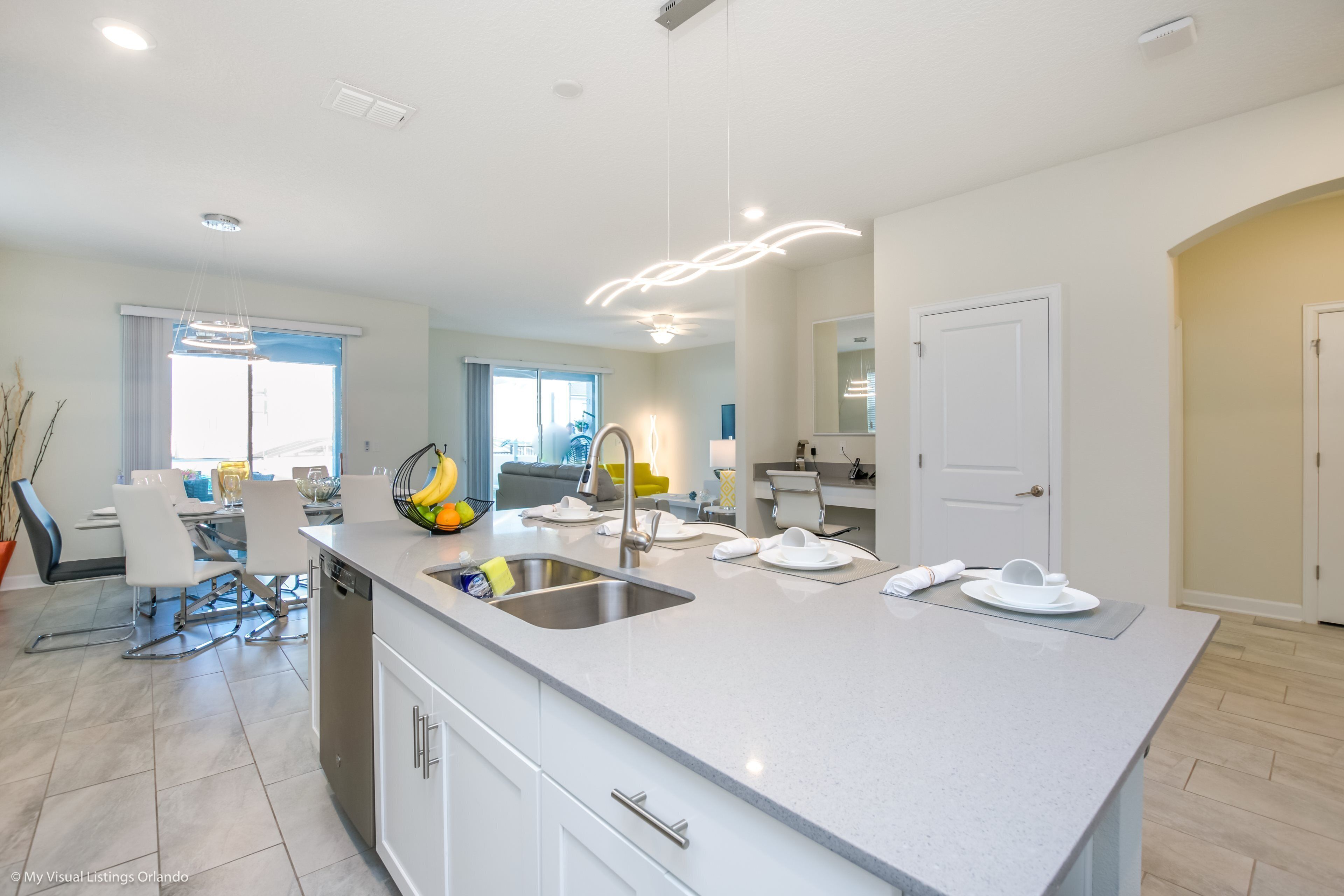 A modern kitchen with a large island, stainless steel sink, and white cabinetry.