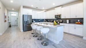 A modern kitchen with white cabinets, stainless steel appliances, and a central island with bar stools. - High End Champions Gate 6 Bdrm (Davenport)