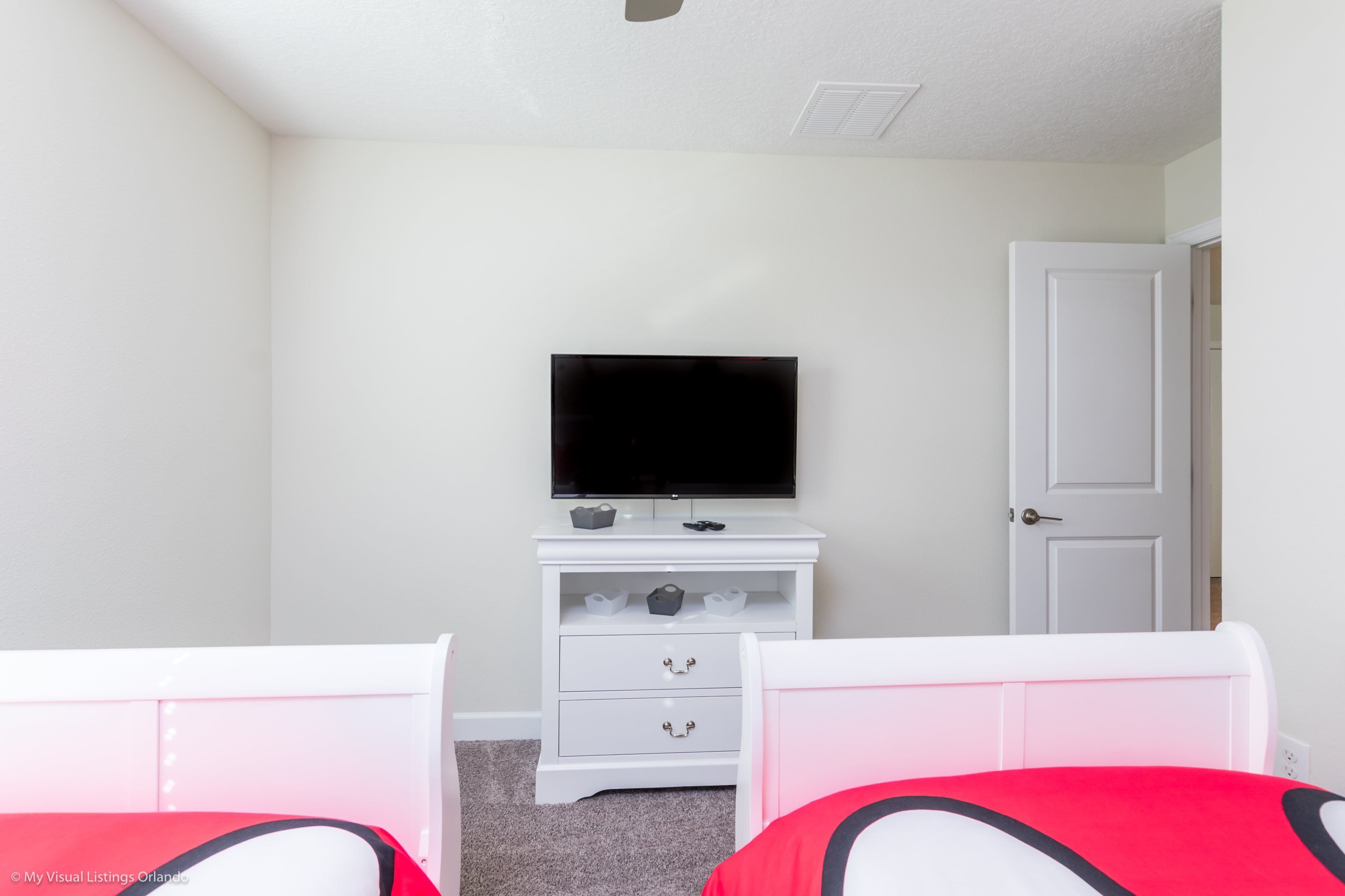 A bedroom with two beds, a white dresser with a TV, and a door.