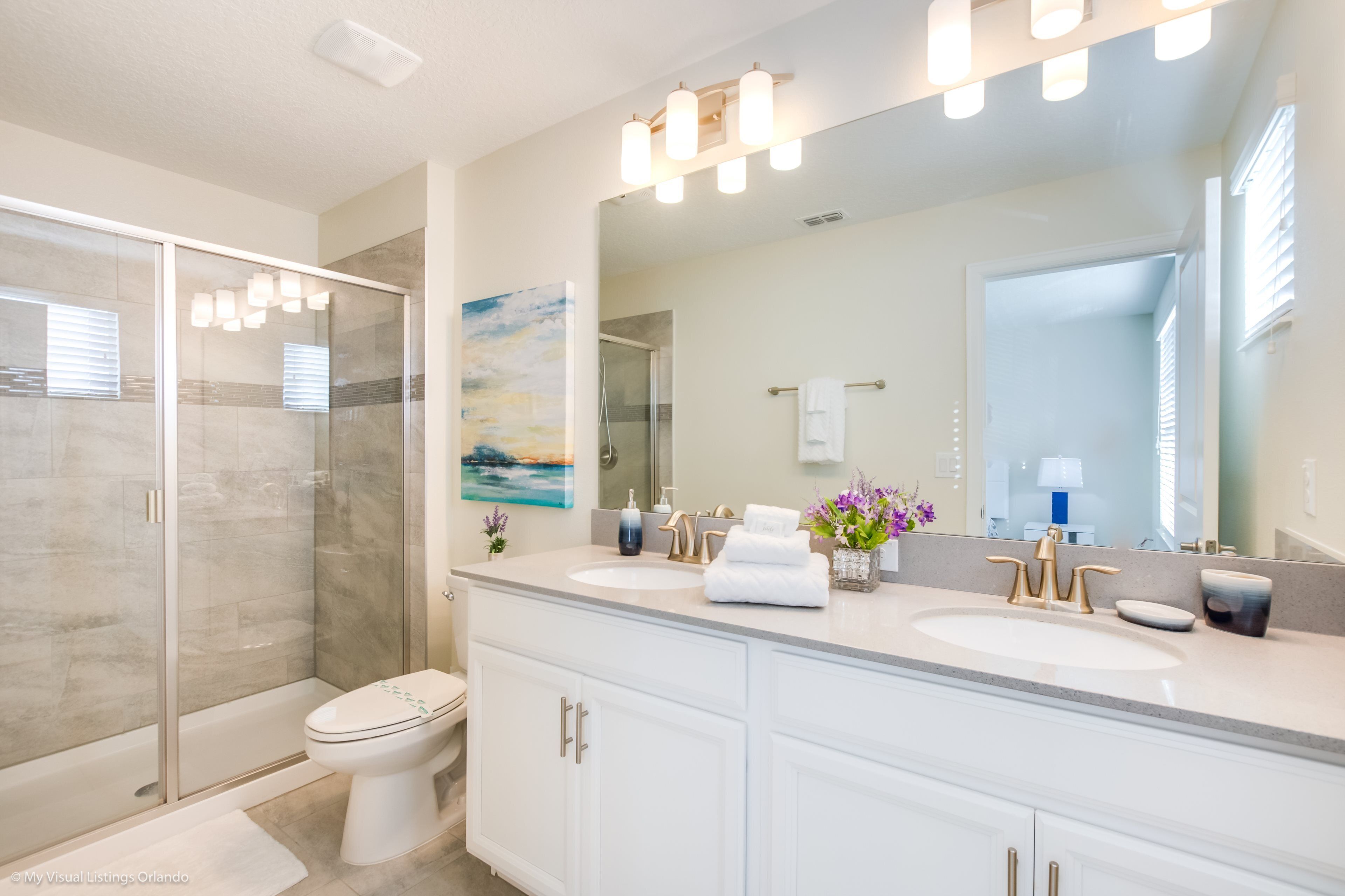 A modern bathroom with a walk-in shower, a toilet, and a vanity with two sinks.