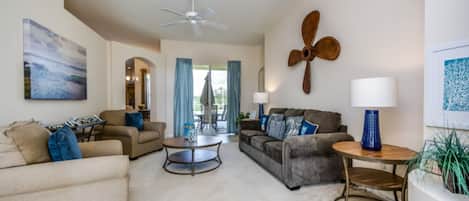A spacious living room with a ceiling fan, a round coffee table, and two sofas with blue cushions.