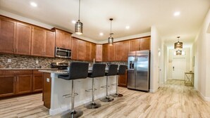 A modern kitchen with wooden cabinets, a central island with bar stools, stainless steel appliances, and a patterned backsplash. - 6bed 4Ba Villa Game Room Pool Spa (Davenport)