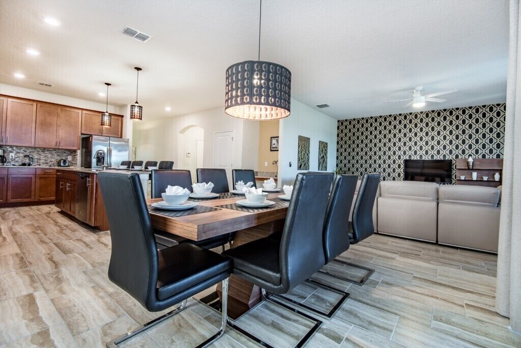 A modern kitchen with wooden cabinets, a stainless steel refrigerator, and a dining area with a wooden table and black chairs.