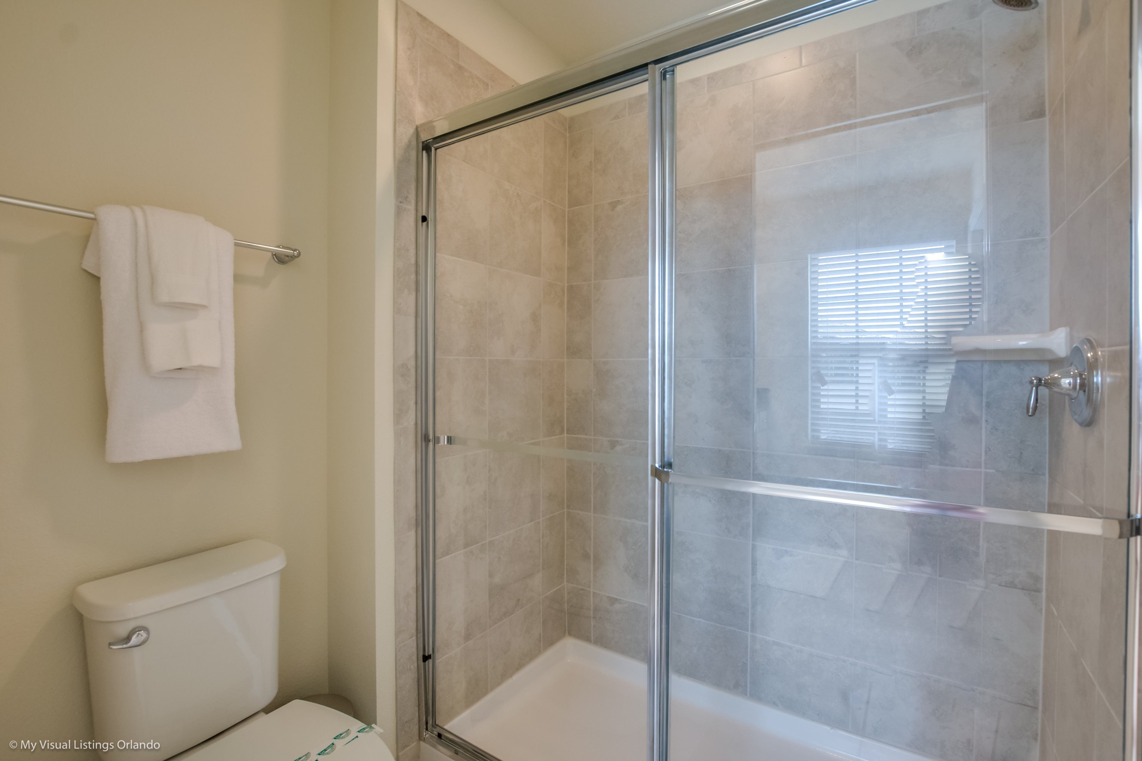 A bathroom with a glass-enclosed shower, a toilet, and a towel rack with two towels.