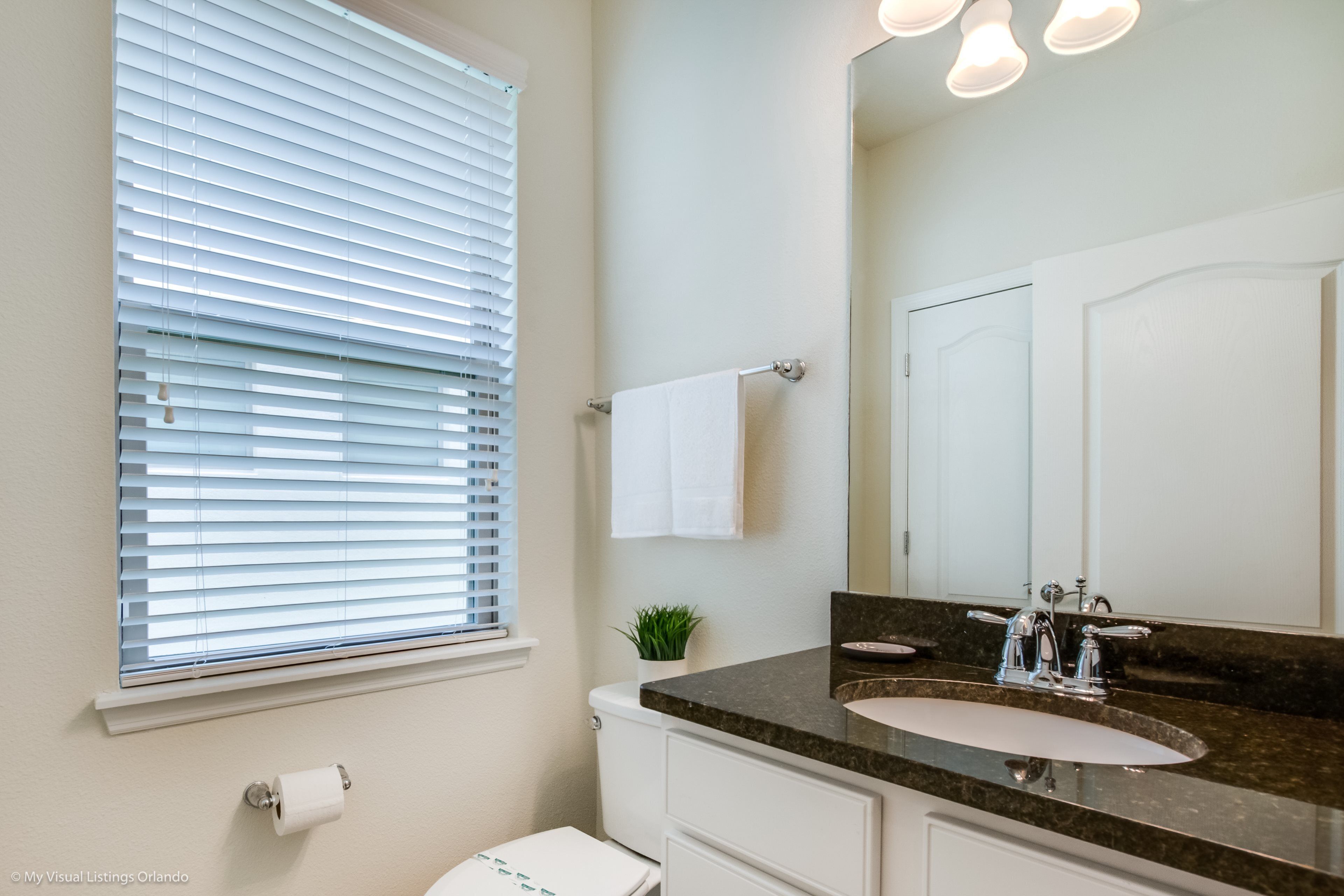 A bathroom with a toilet, sink, mirror, and window with blinds.