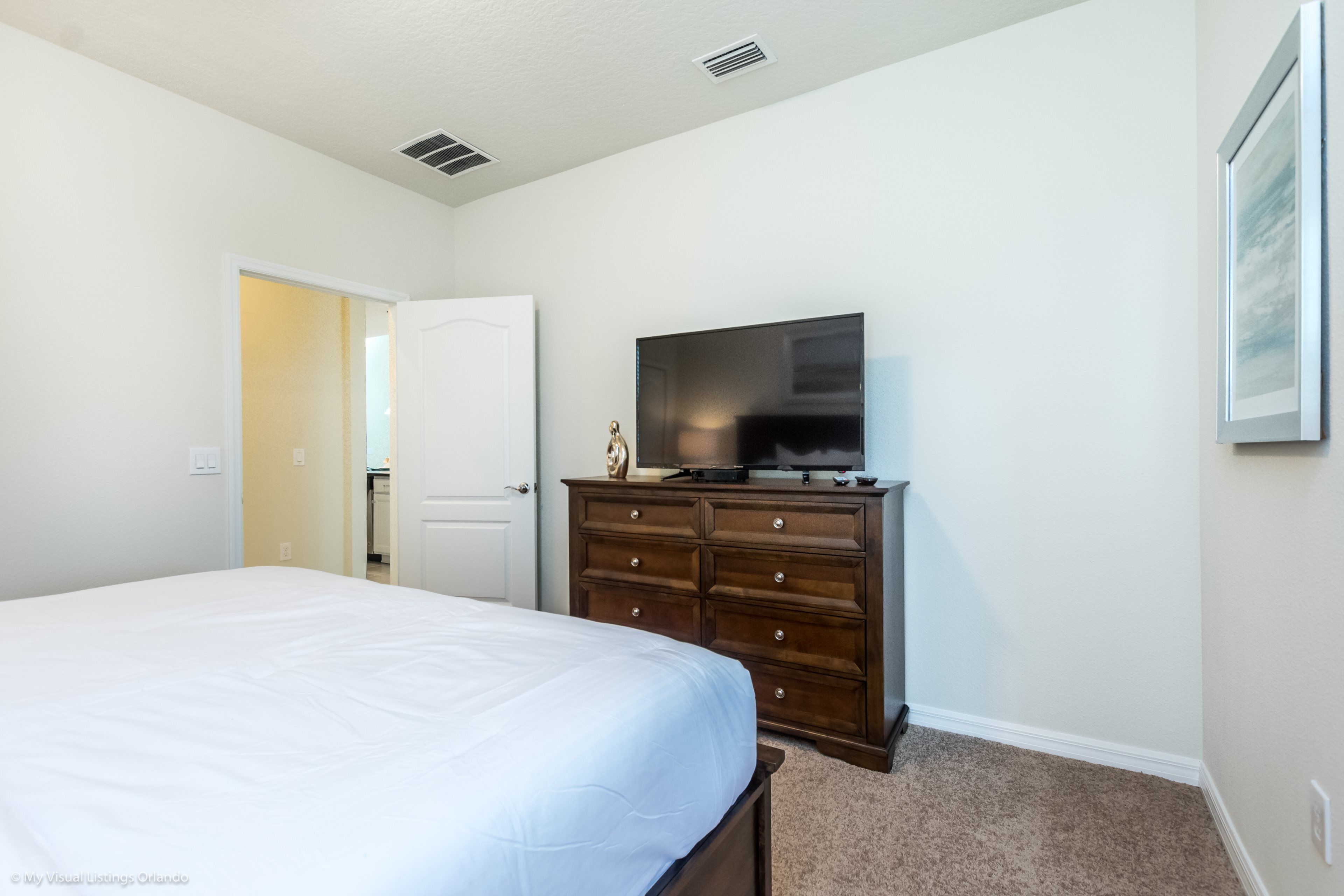 A bedroom with a bed, a dresser, a television, and a door leading to another room.