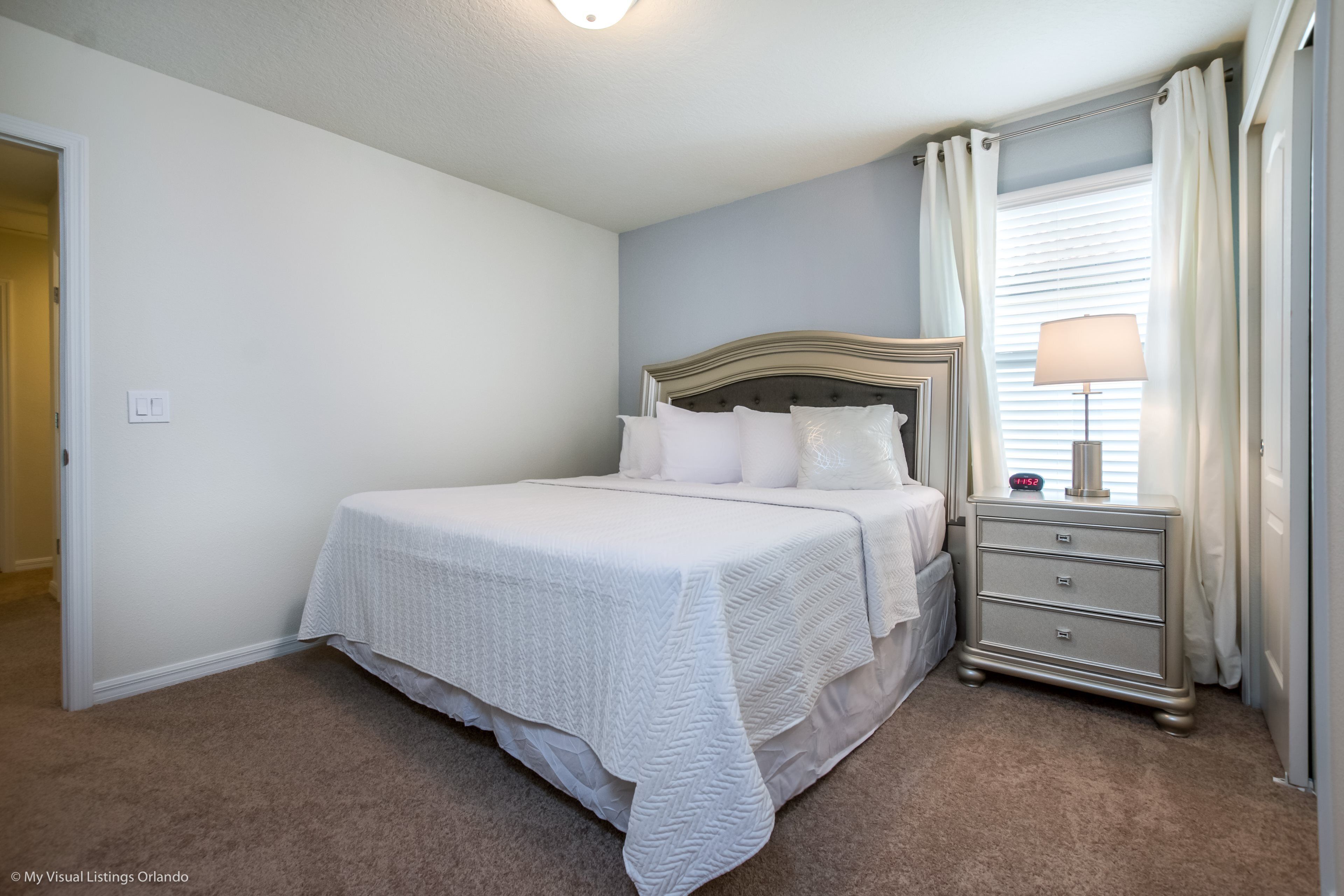 A bedroom with a bed, nightstand, lamp, and curtains.