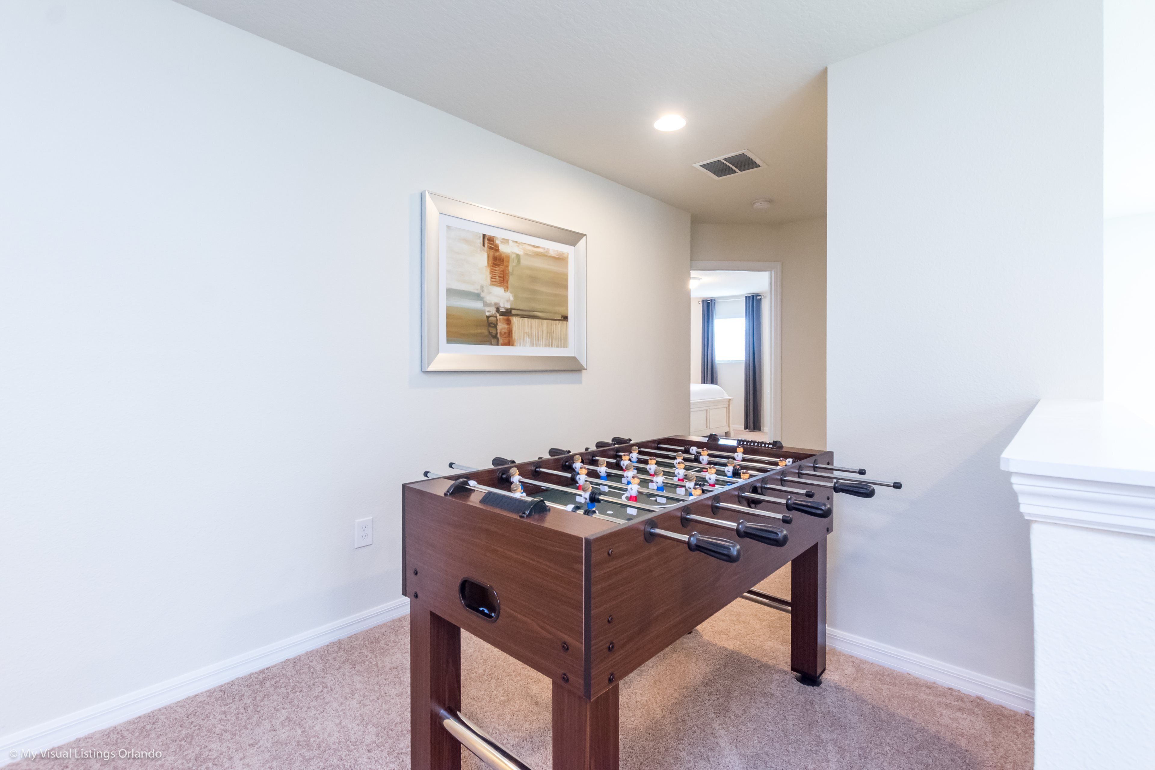 Quarto com mesa de futebol de mesa, quadro na parede e porta para outro cômodo.