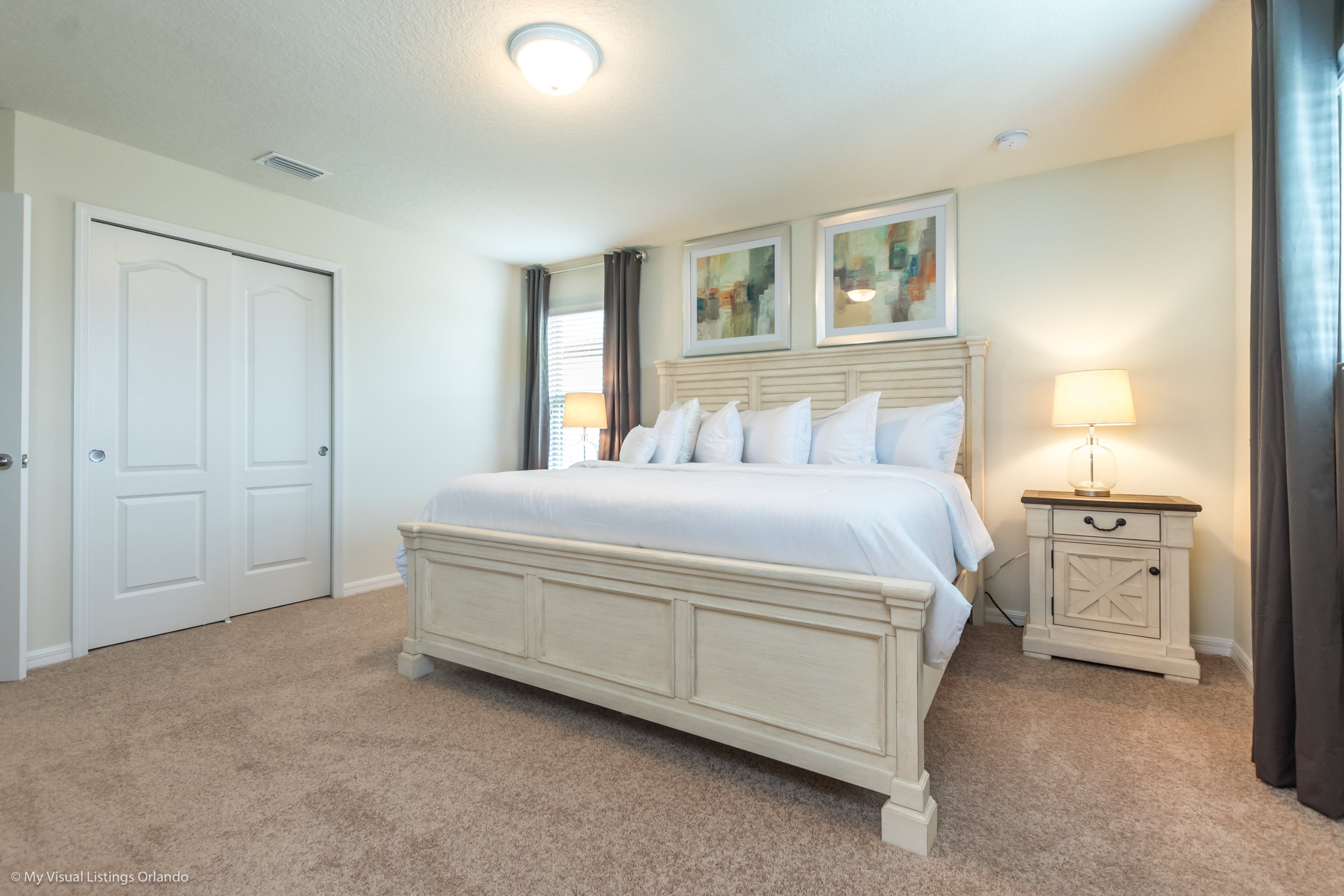 A bedroom with a large bed, a nightstand with a lamp, and two framed pictures on the wall.