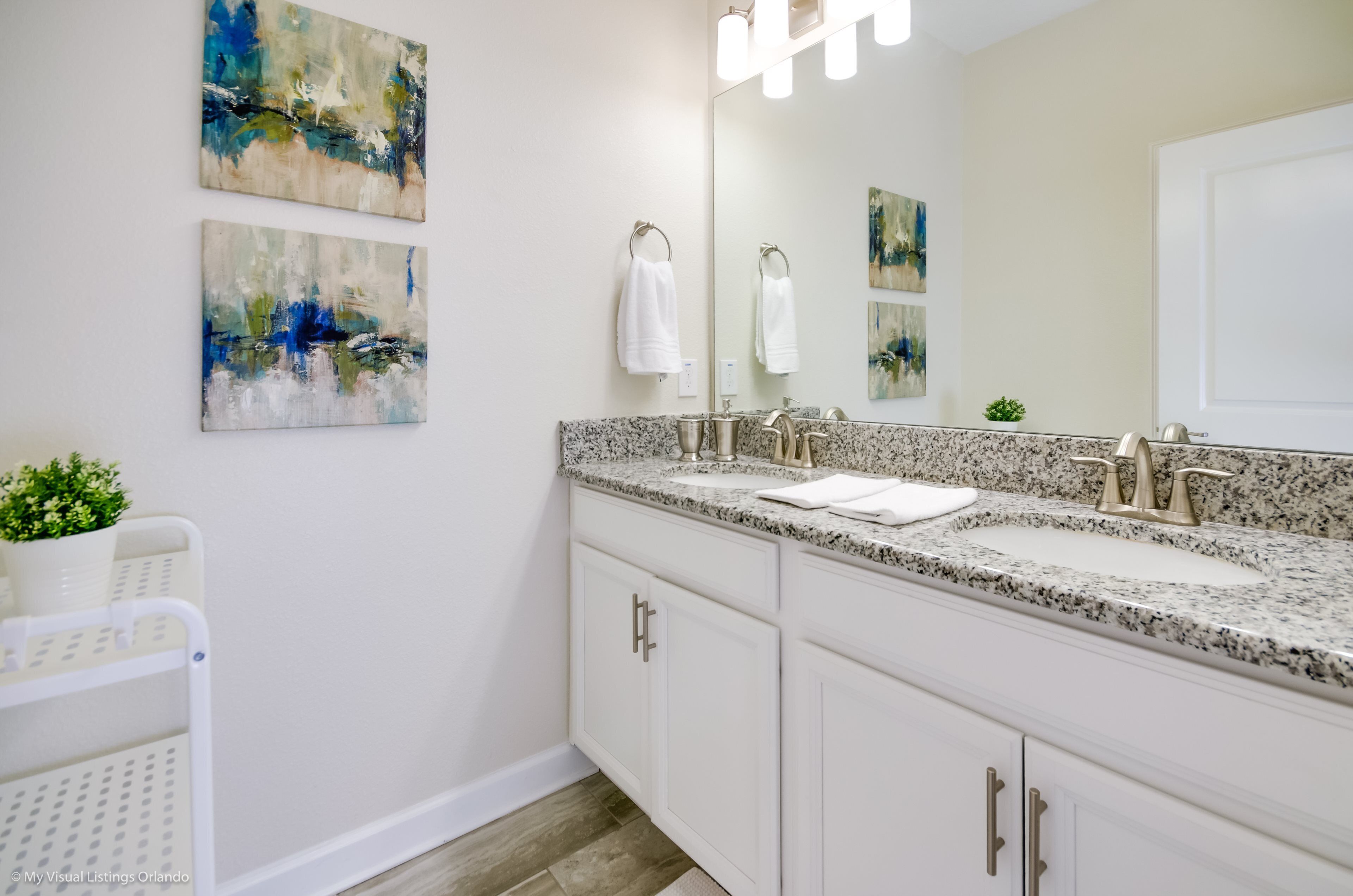 A modern bathroom with a double sink, white cabinets, and abstract art on the walls.
