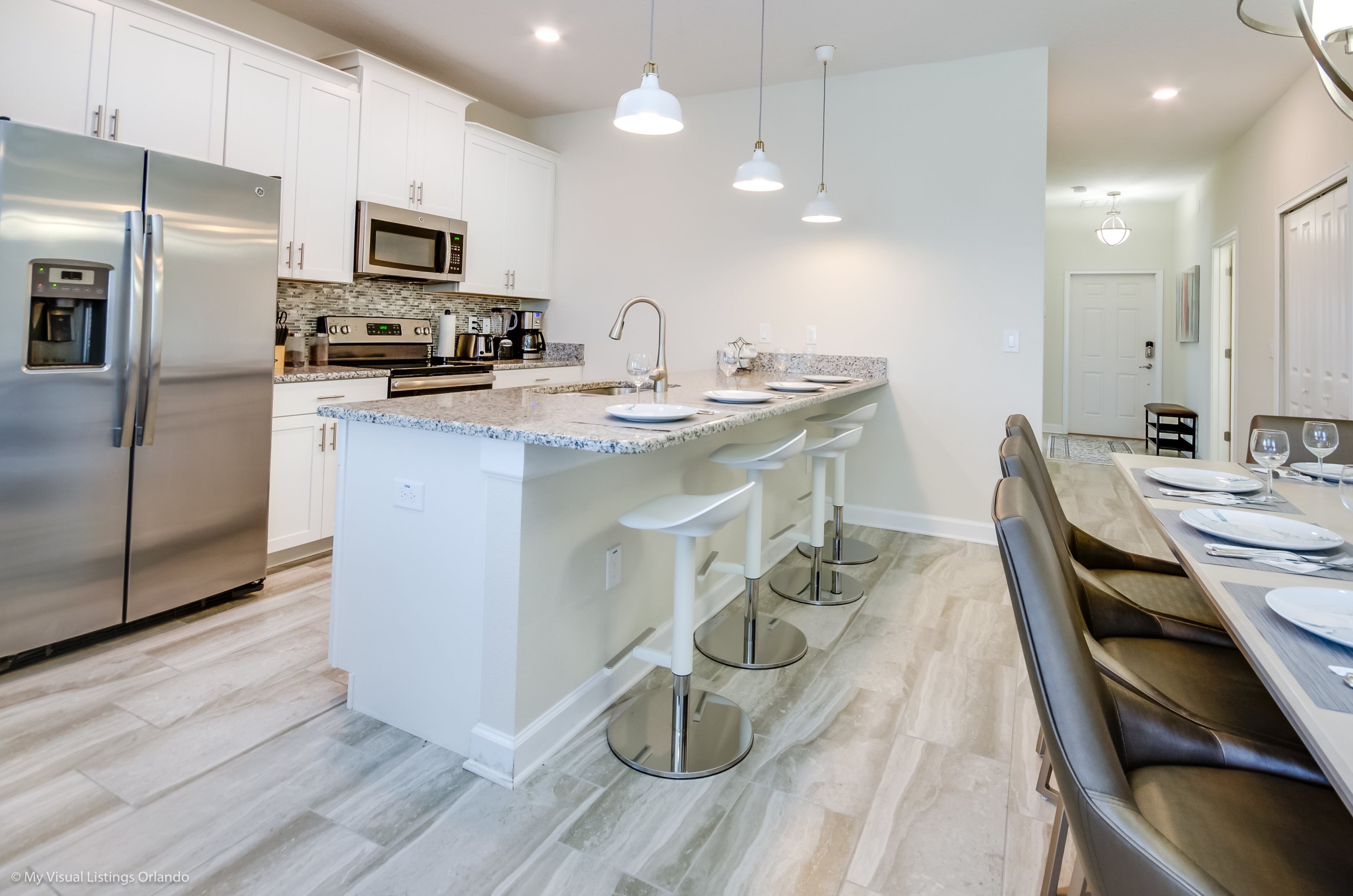 Una cocina moderna con armarios blancos, electrodomésticos de acero inoxidable, encimera de granito y una zona de bar con taburetes.