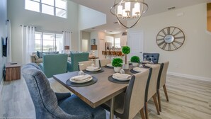 Un coin repas avec une table en bois dressée pour quatre personnes, entourée de chaises. Un lustre est suspendu au-dessus de la table, et une horloge est fixée au mur.