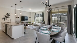 Eine moderne Küche mit Kochinsel, Essbereich mit rundem Tisch und einem großen Fenster mit Vorhängen.