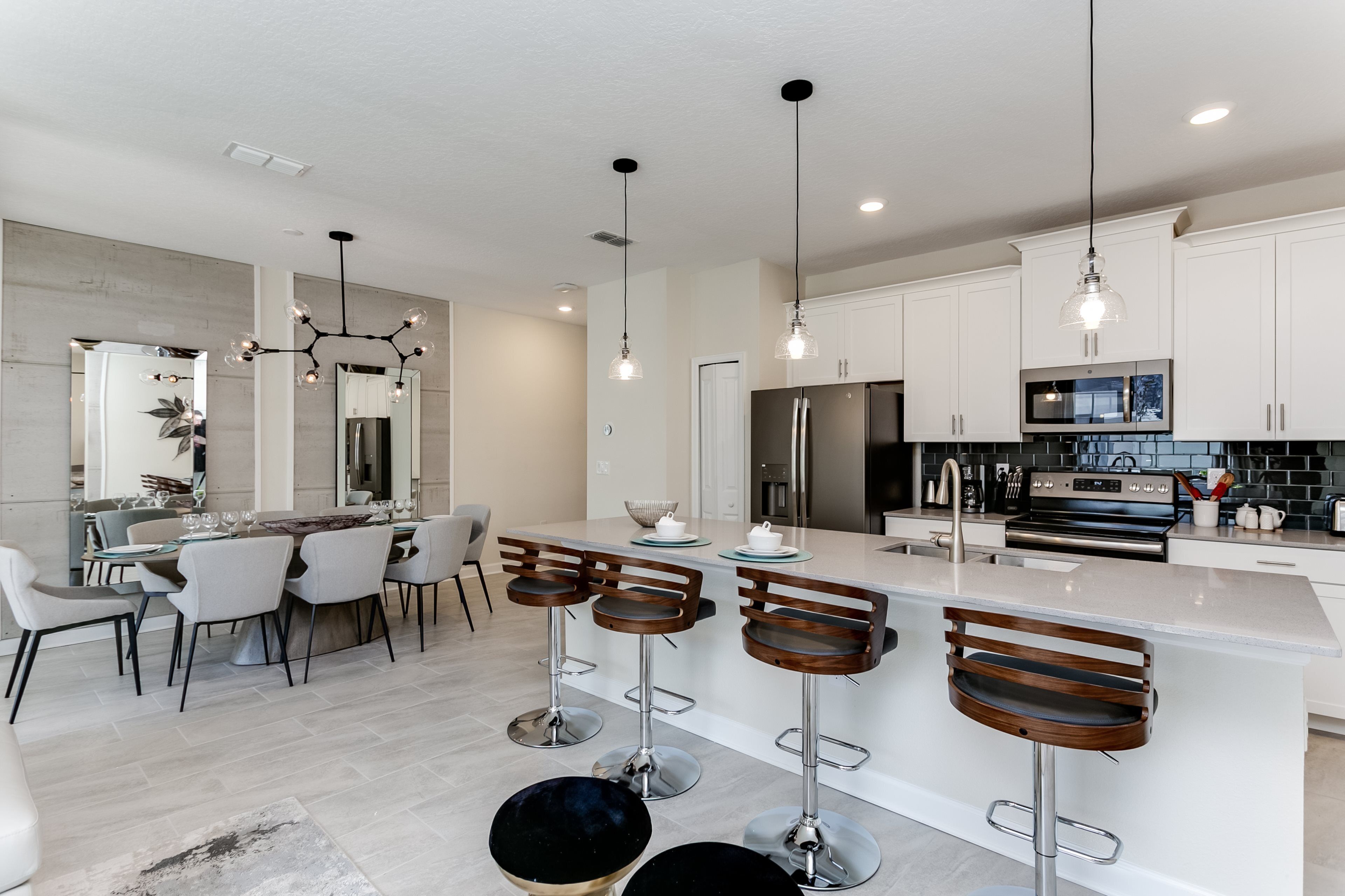 A modern kitchen with white cabinets, a central island with bar stools, stainless steel appliances, and pendant lighting.