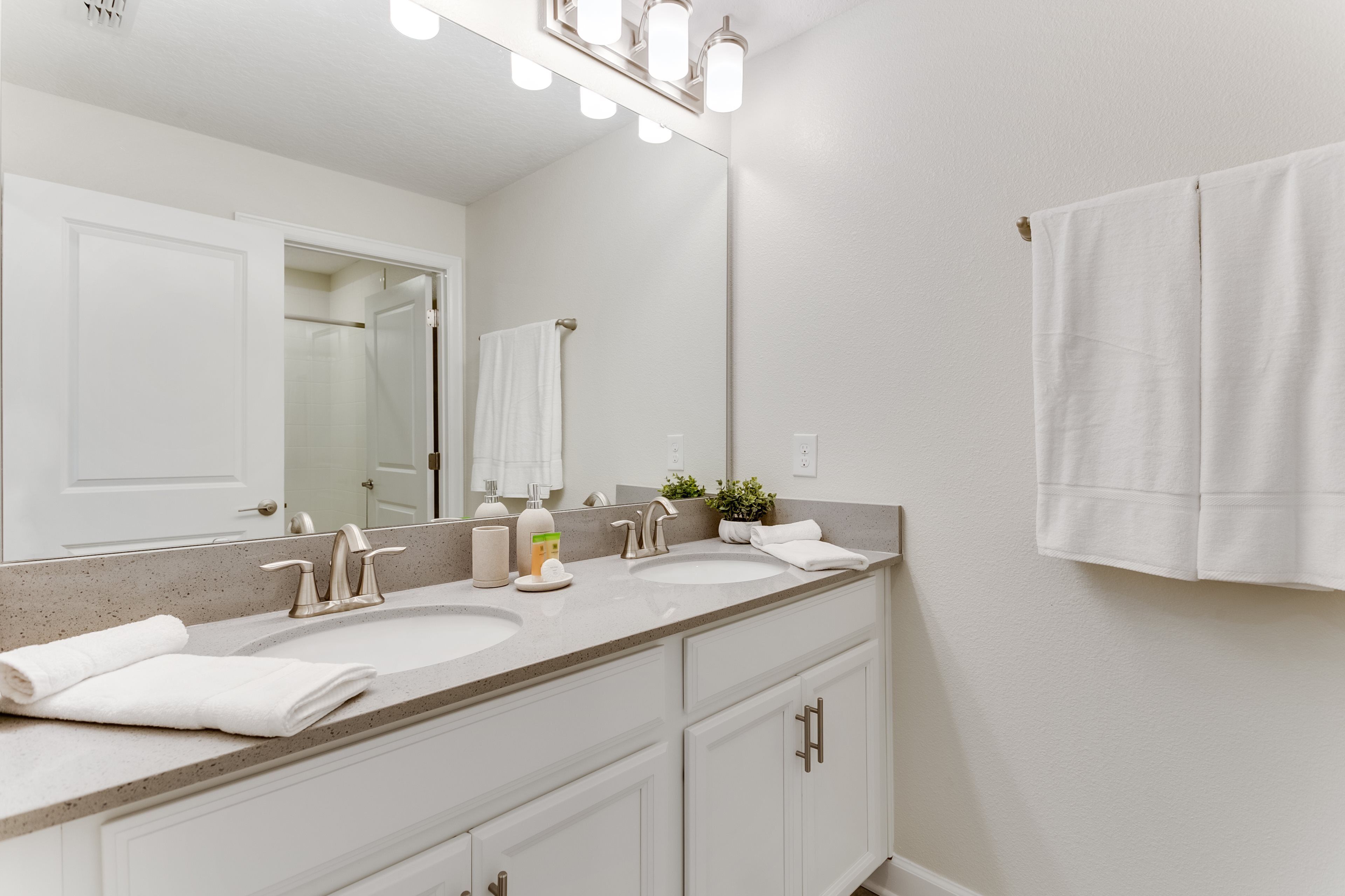 A bathroom with two sinks, a large mirror, and white cabinets.