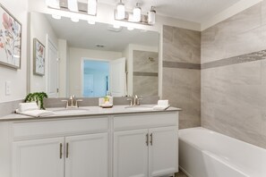 A modern bathroom with a double sink vanity, a large mirror, and a bathtub. - 4bed 3Ba Storey Lake Home w. Pool (Kissimmee)