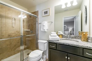 Et moderne badeværelse med et glasafskærmet brusebad, toilet, vaskebord med vask og et spejl.