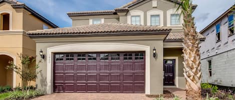 A two-story house with a large garage door, a well-maintained driveway, and a palm tree in the front yard.