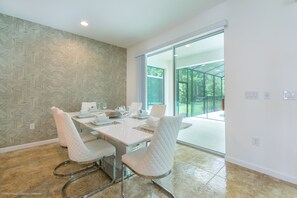 A modern dining area with a white table and chairs, a patterned wall, and a large glass door leading to an outdoor space.