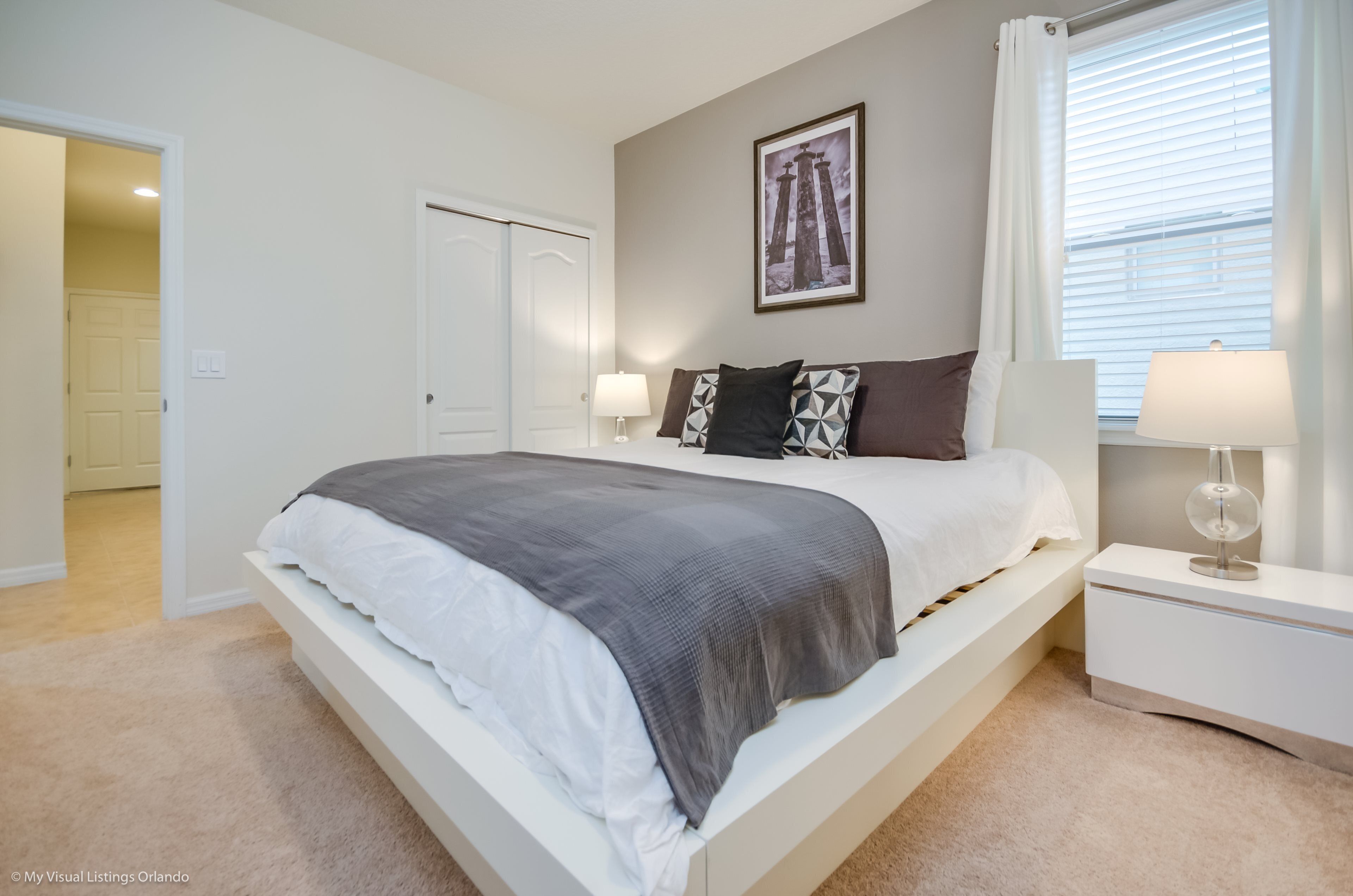 A bedroom with a bed, bedside tables, a door, and a window with blinds.