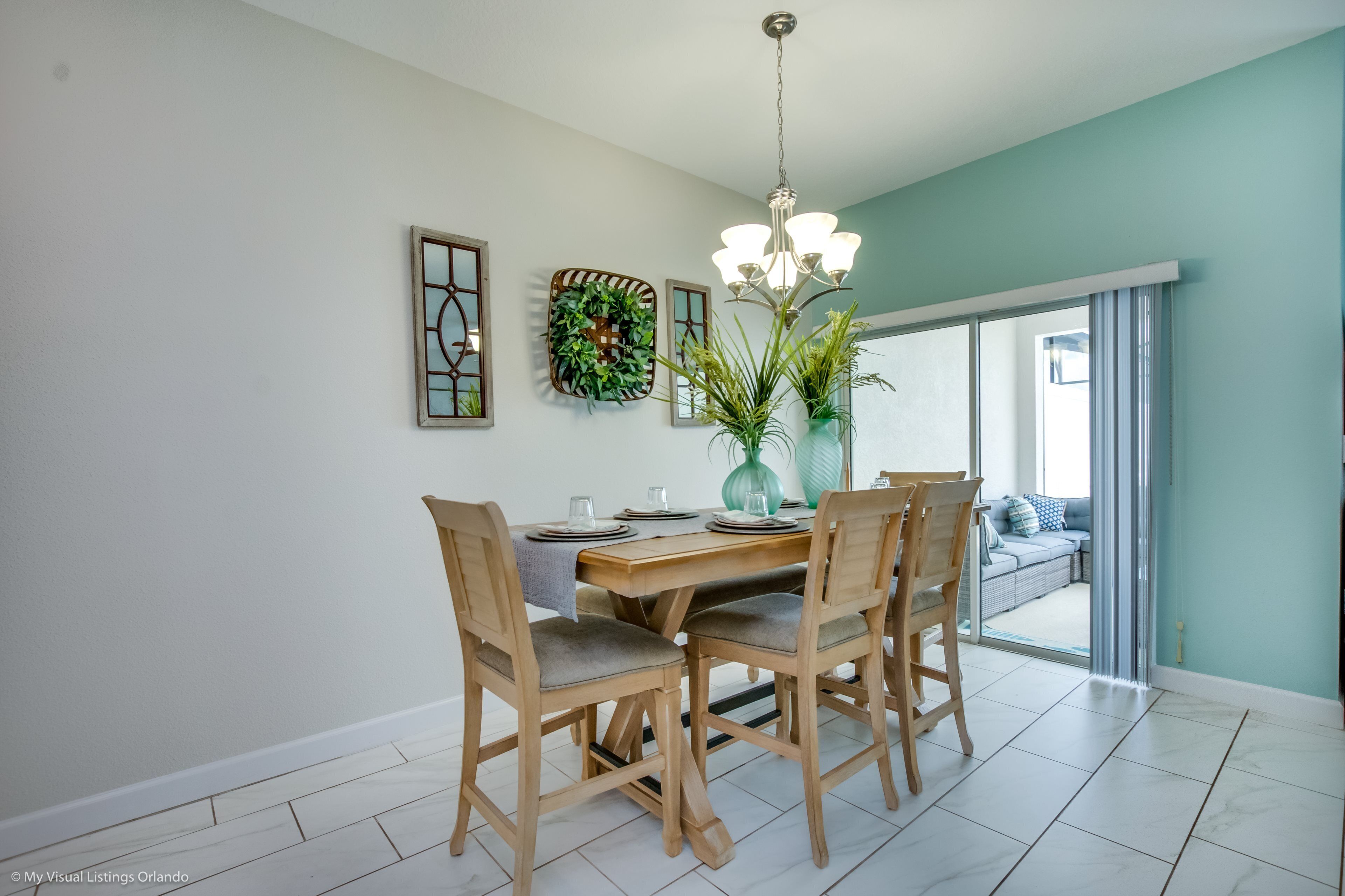A dining area with a wooden table, four chairs, a chandelier, and a view of a balcony.