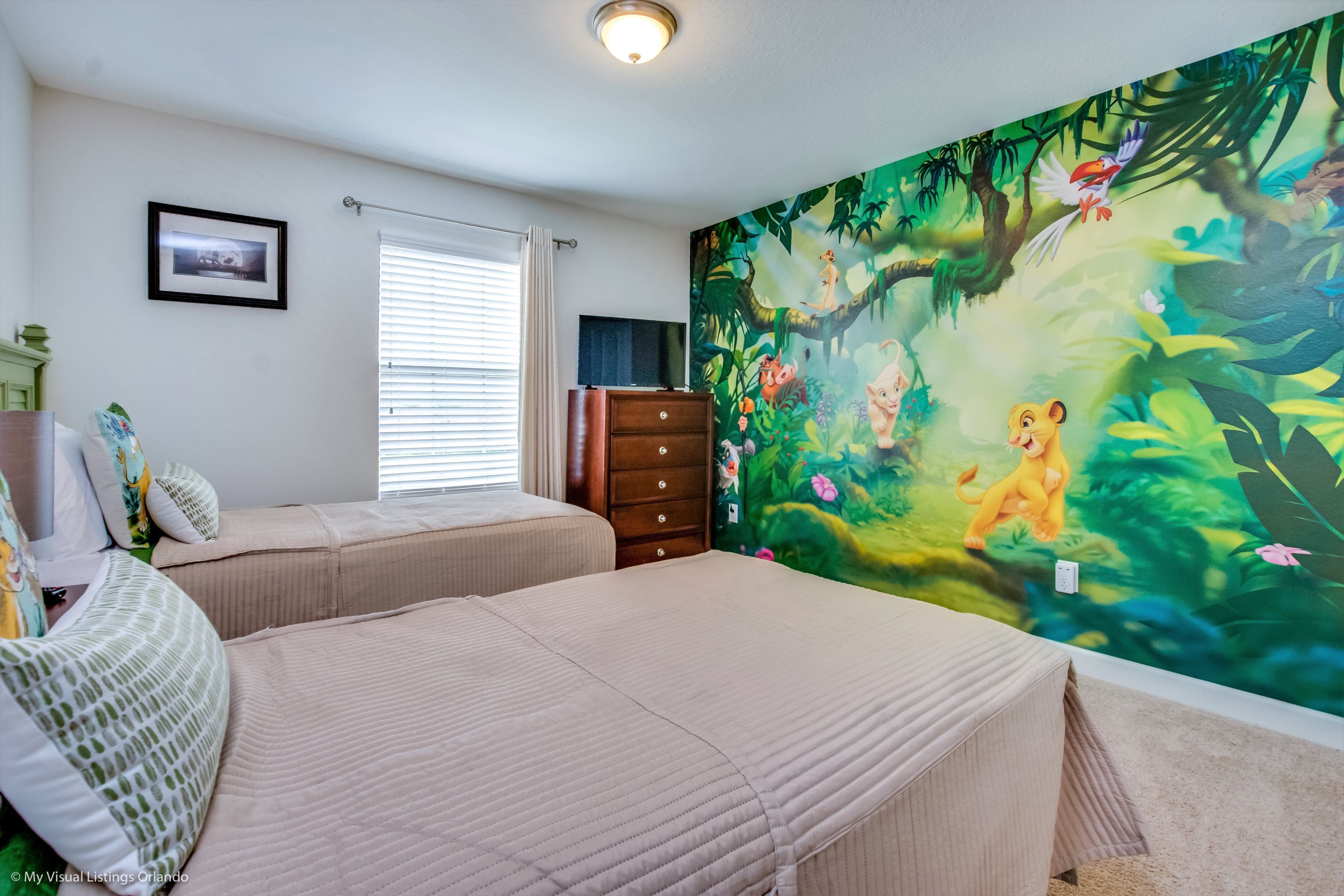 A bedroom with two beds, a dresser, a window with blinds, and a jungle-themed mural on the wall.