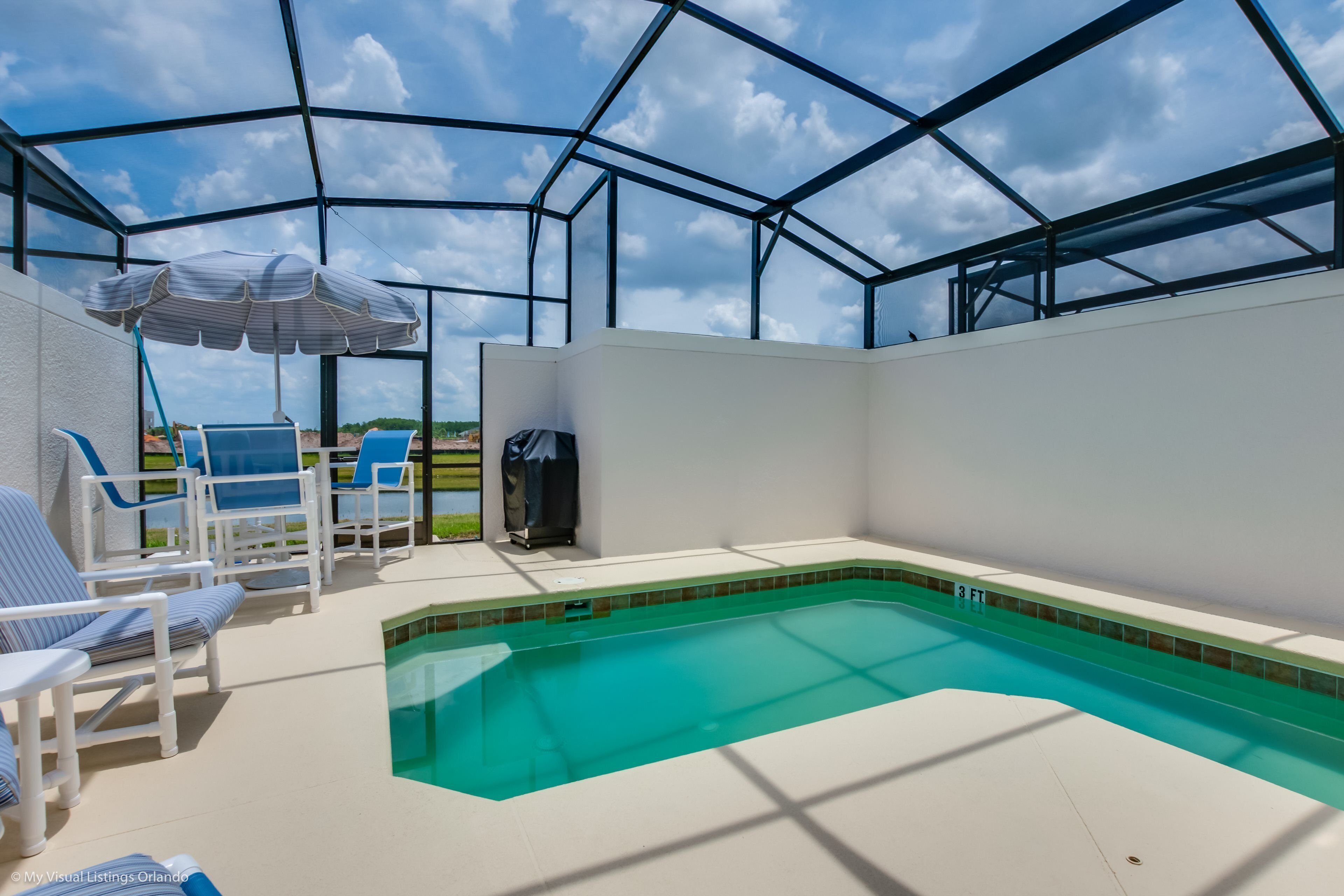 A covered outdoor swimming pool with blue lounge chairs and a striped umbrella.