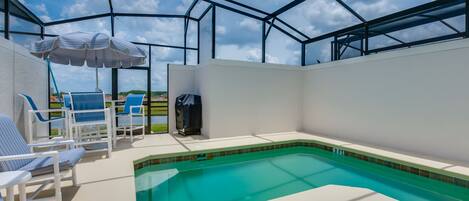 A covered outdoor swimming pool with blue lounge chairs and a striped umbrella.
