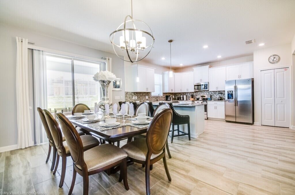 A modern kitchen with white cabinets, stainless steel appliances, and a dining area with a chandelier.