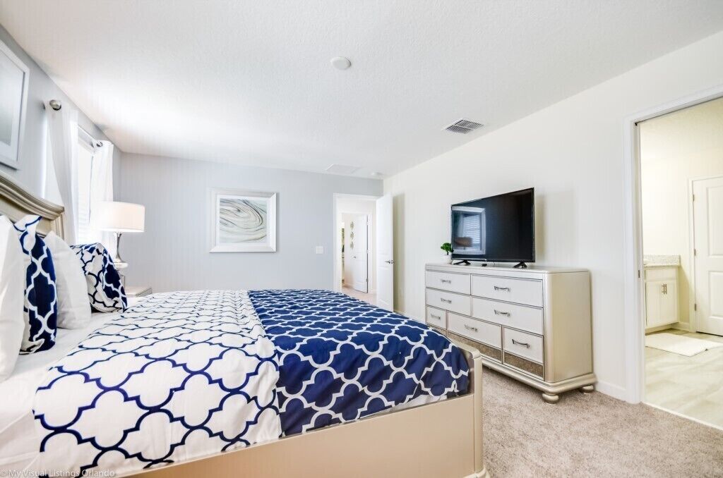 Un dormitorio con cama, cómoda, televisor y puerta que da a otra habitación.