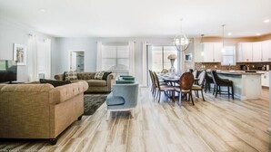 Un salon spacieux avec un canapé, un coin repas comprenant des chaises et une table, et une cuisine équipée de placards et d’un plan de travail.