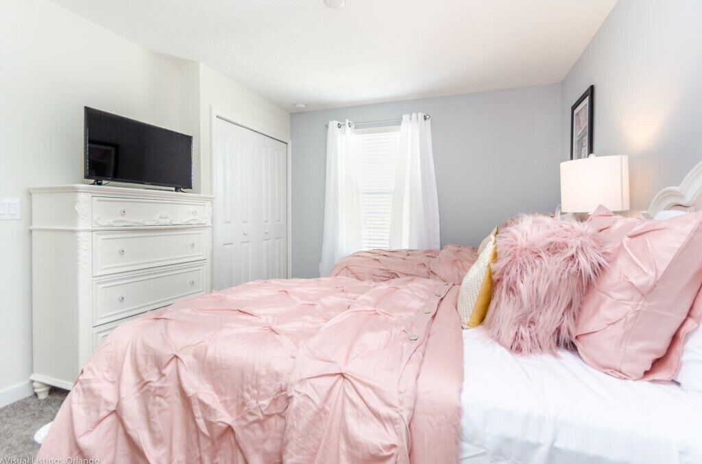 A bedroom with a bed, a dresser, a television, and a window with curtains.