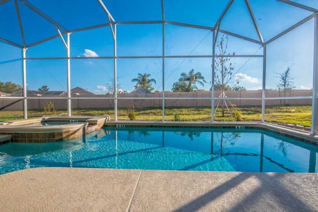 A swimming pool with a clear view of the surrounding landscape, including a fence and distant trees.