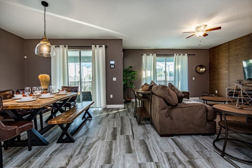 A modern living room with a dining area, featuring a wooden dining table, benches, a sofa, and a ceiling fan.