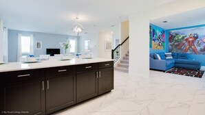Een moderne keuken met donkere kastjes en een wit aanrecht, een woonruimte met een blauwe bank en een kleurrijke muurschildering, en een trap naar een ander niveau.