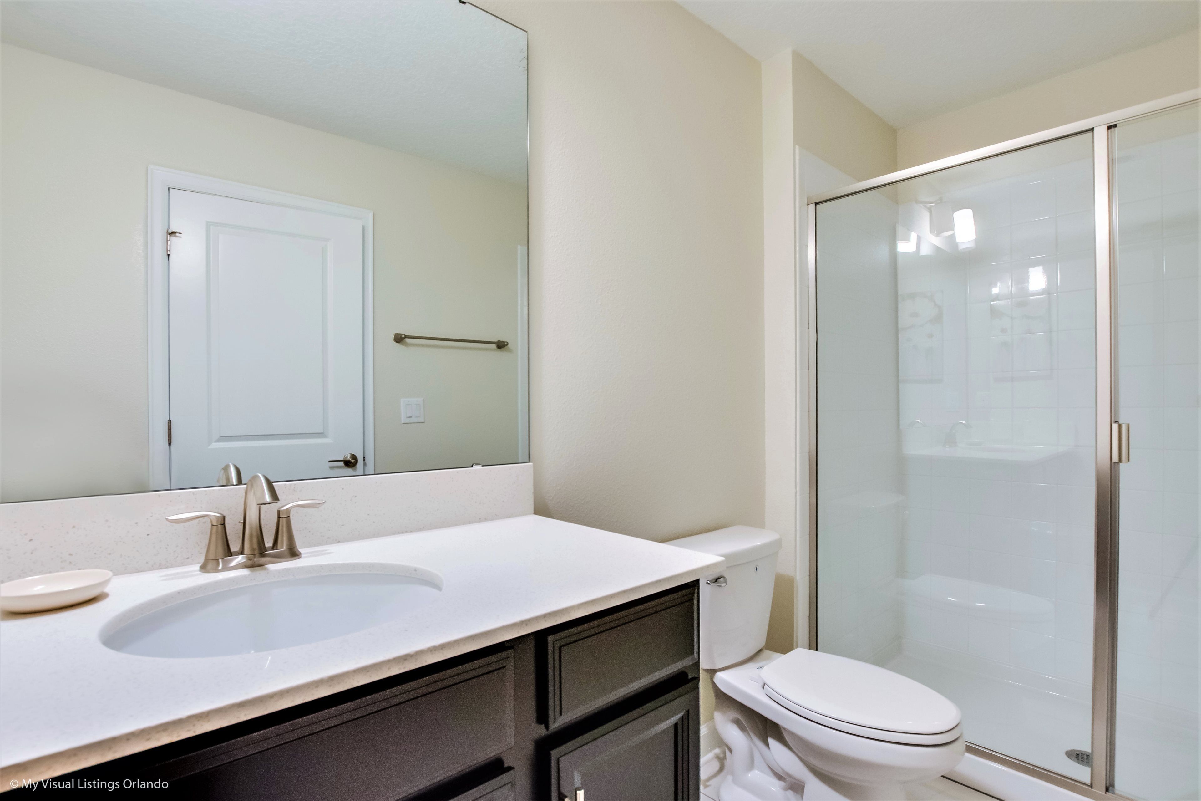 A bathroom with a white sink, a mirror, a toilet, and a glass shower enclosure.