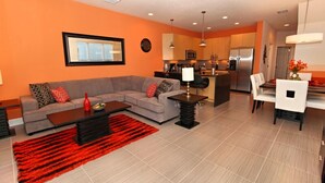 Una sala de estar moderna con un sofá gris, un tapete rojo y un comedor con sillas blancas y una mesa.