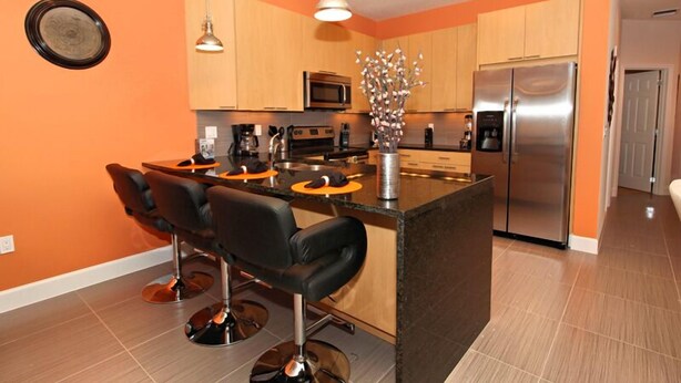 Una cocina moderna con armarios de madera, un refrigerador de acero inoxidable y una isla central con taburetes de bar.
