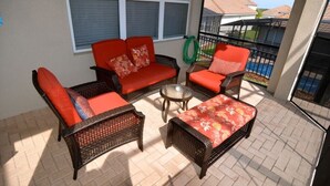 A sunlit patio with wicker furniture, a glass table, and a view of a residential area. - 7783tb Windsor Hills Resort 5 Bed 5 Bath (Kissimmee)