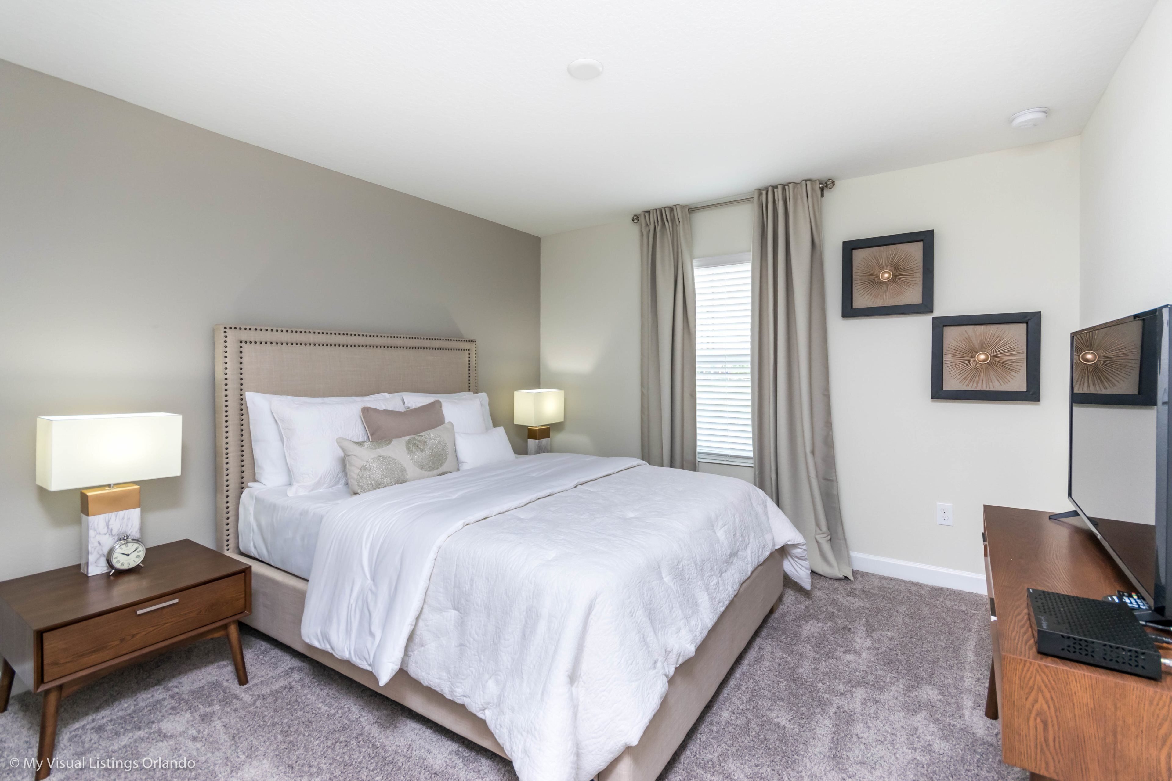 A bedroom with a bed, nightstand, lamp, and a desk with a computer.
