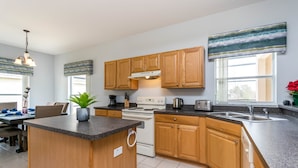 A modern kitchen with wooden cabinets, a central island, and a dining area with a table and chairs. - 946bd Amazing High End Gated (Davenport)