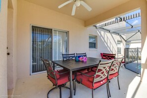 Eine überdachte Terrasse mit Tisch und Stühlen, einem Deckenventilator und einer Schiebetür.
