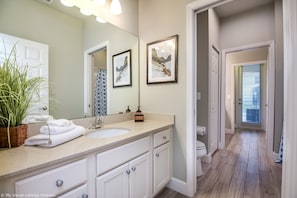 Une salle de bain avec un grand miroir, deux œuvres d’art encadrées, un lavabo et des toilettes.