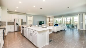 A spacious kitchen with white cabinets, a large island, and a dining area with a white sofa and table. - Fabulous 9 Bed 6,5 Ba Villa Games, Pool & Spa 9063srl (Kissimmee)